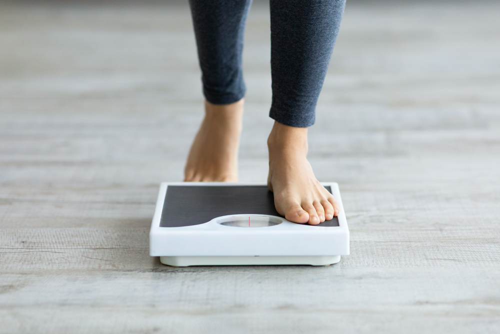 Unrecognizable young Indian woman stepping on scales to measure her weight at home, closeup of feet. Cropped view of millennial lady checking result of her slimming diet. Healthy living concept
