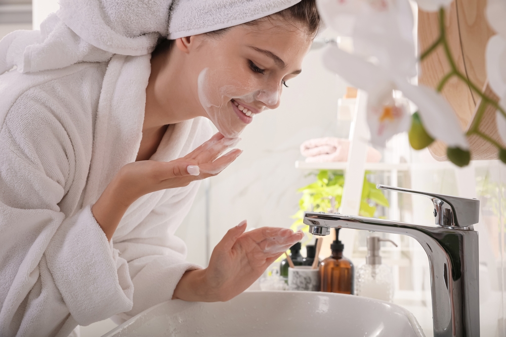 Beautiful teenage girl applying cleansing foam onto face in bathroom. Skin care cosmetic
