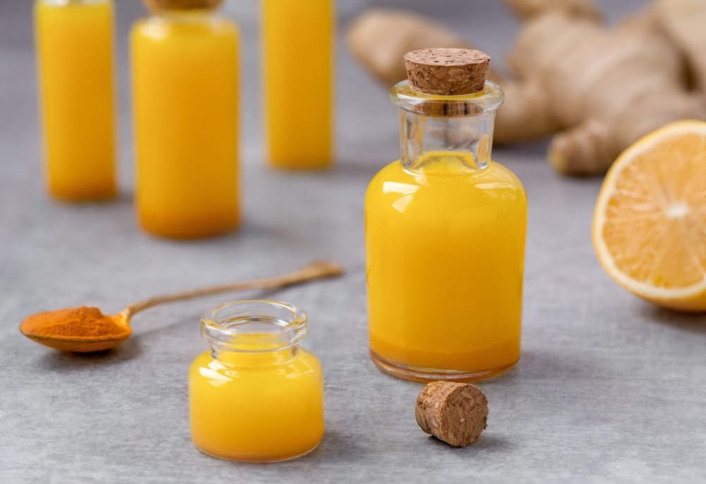Lemon Ginger Turmeric Shots. Fresh portion of ginger root, lemon juice and turmeric powder drink in a small glass bottles with ingredients on background. Close up, selective focus.
