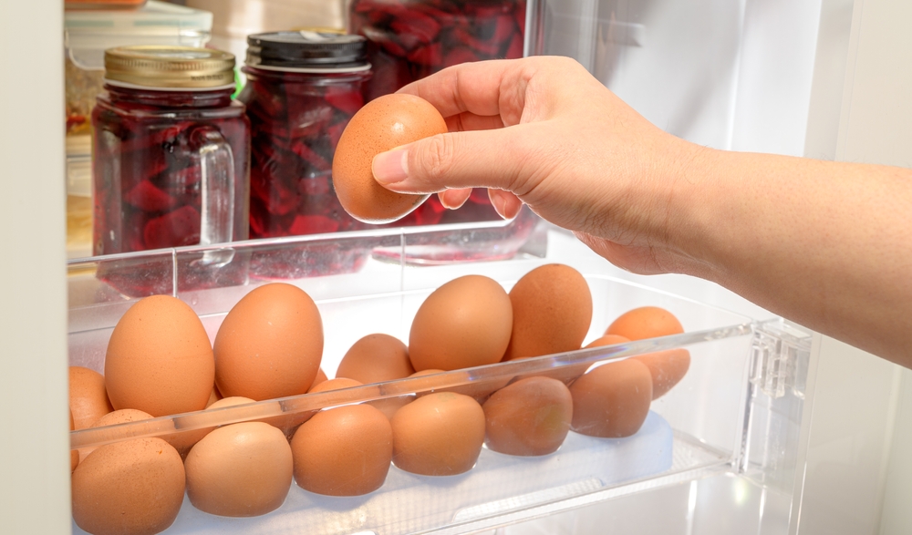 Hands to organize brown eggs on the refrigerator shelf.