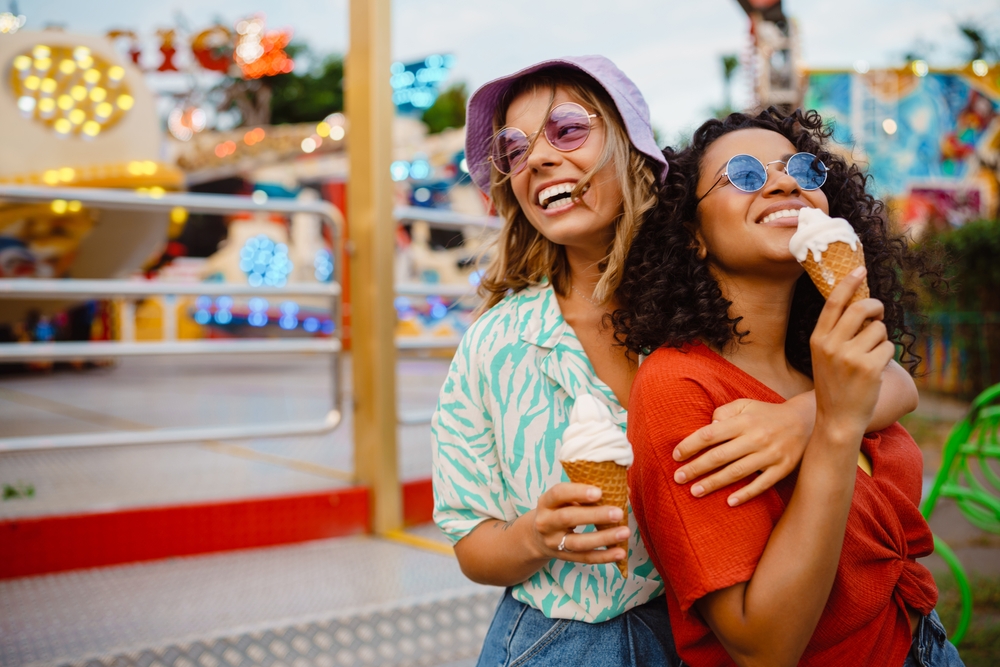 Young multiracial women eating ice cream while spending time in attraction park