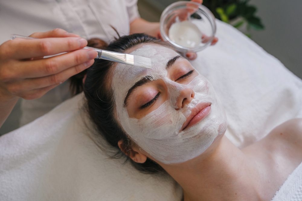 Woman getting facial care by beautician at spa salon. Face peeling mask, spa beauty treatment, skincare.
