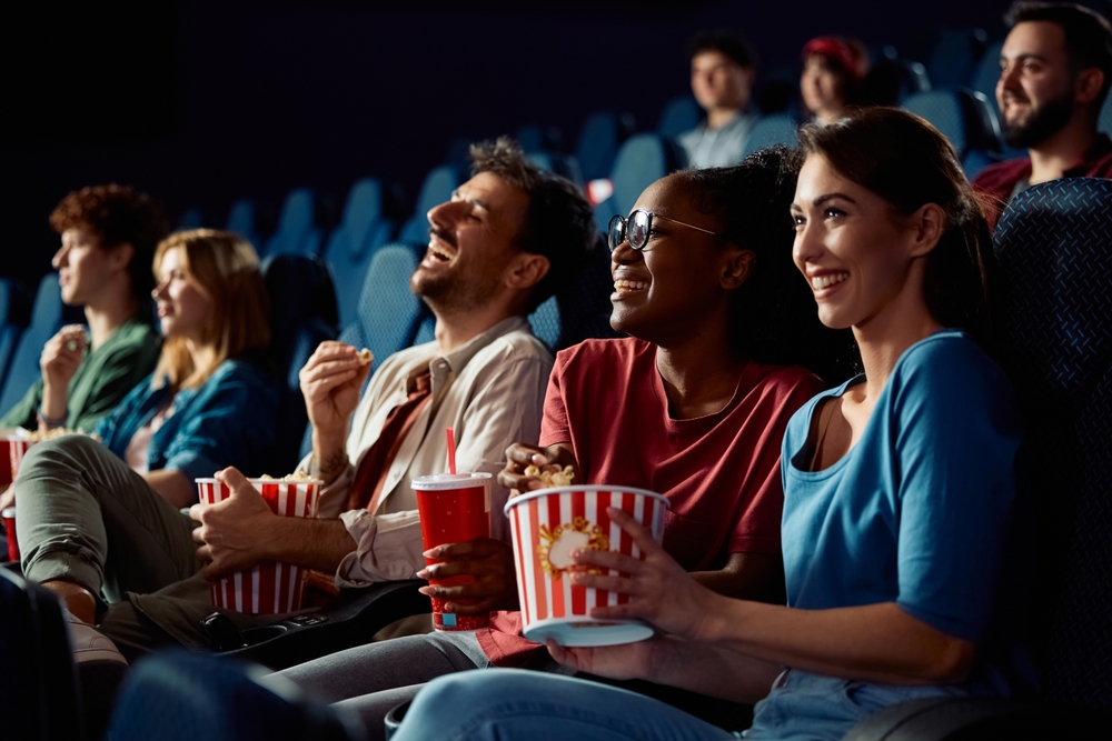 Happy friends enjoying in movie projection in theater. Focus is on African American woman eating popcorn.