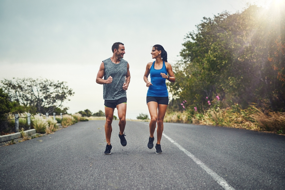 Couple, road and smile with running for fitness for training, support and love in California. Workout, exercise and people with jogging for health or wellness and wellbeing in morning with lens flare
