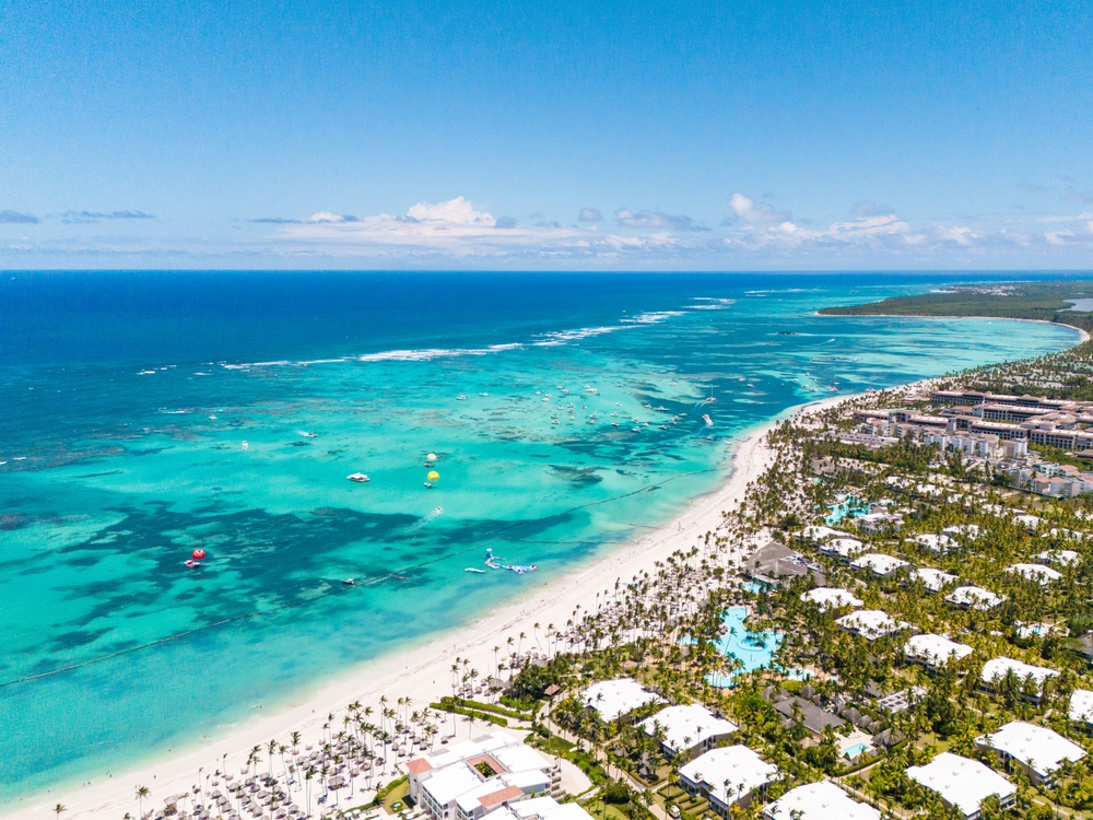 Aerial view of white sand beach with many all inclusive hotels in Punta Cana. Turquoise water, tall palm trees and straw umbrellas on the coast. Best place for summer vacations
