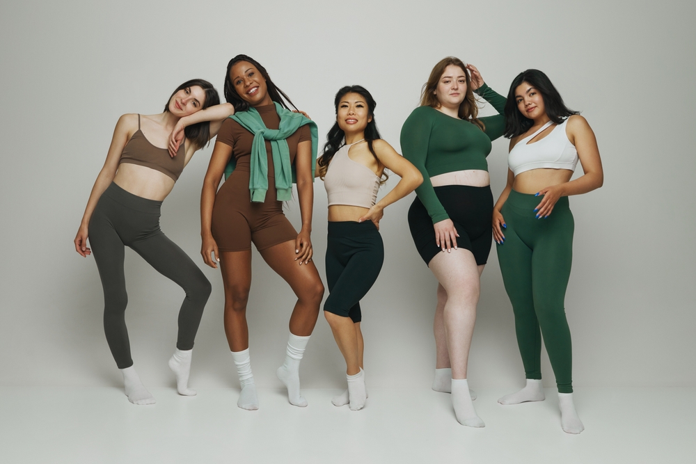 Diverse group of five women standing together in athleisure wear, showcasing different body types and ethnic against white background. Concept of beauty, support, unity, wellness, body positivity.
