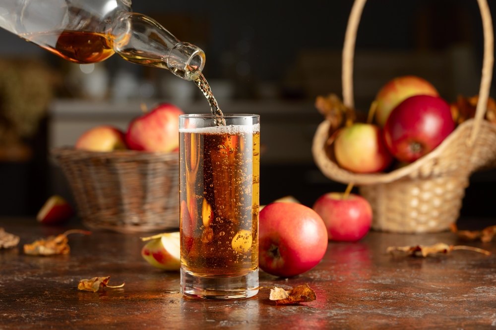 Apple cider is poured from a bottle into a glass. Fresh drink with apples on an old kitchen table.
