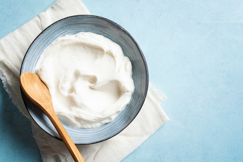 Homemade Greek Yogurt in bowl on blue background, top view, copy space. Organic plain greek yogurt, labneh cream cheese, sour cream for healthy breakfast.