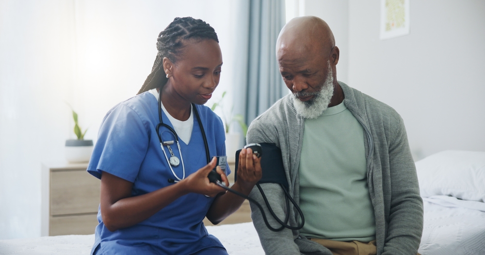 Hospital, senior man and nurse with monitor for blood pressure, medical test or cardiovascular. Black people, mature patient or caregiver for hypertension diagnosis, healthcare or consultation in bed

