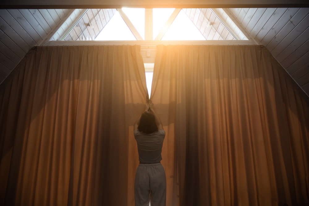 Woman is closing big curtains in modern house.