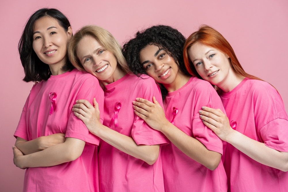 Diverse group of women of different ages and ethnicities are standing together, wearing pink t-shirts with pink ribbons, symbolizing their support for breast cancer awareness
