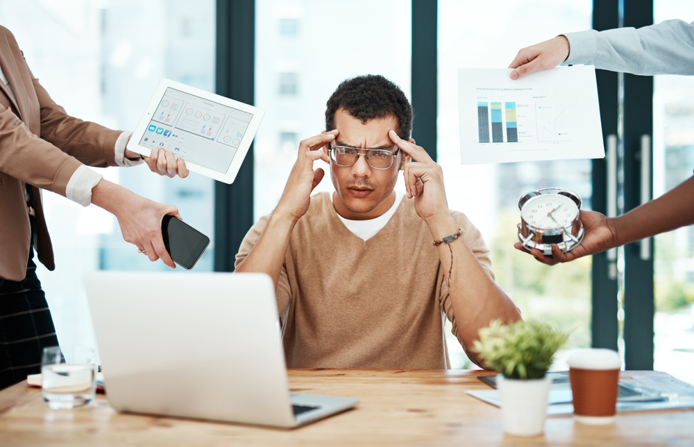 Man, headache and group with hands, office and burnout with charts, laptop and tired with phone. Person, frustrated and time management with reminder, tablet and sales report with at creative agency
