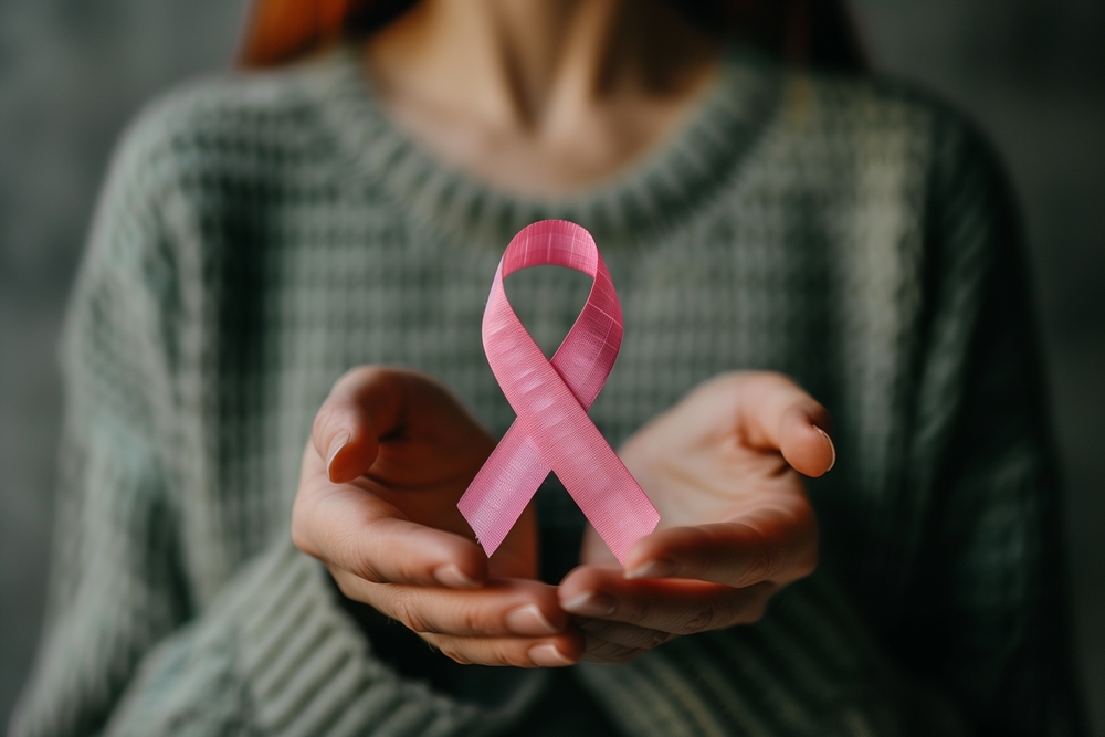 Close-up of a woman's hands holding a pink ribbon, symbolizing cancer awareness and support for women's health.