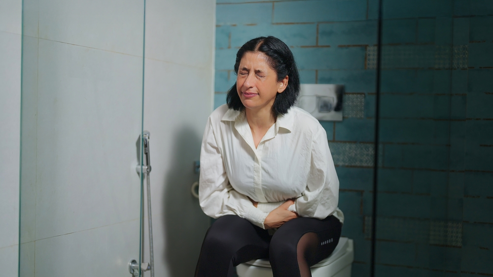 Indian old aged senior upset sad worried woman sitting on toilet bowl hold painful belly stomach feel hurt abdomen chronic ache suffer from indigestion flatulence facing abdominal problem indoor house