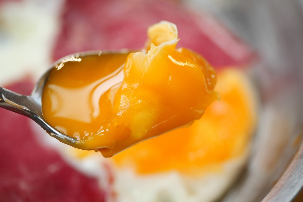 CloseUp of a Spoon with a Runny Egg Yolk on Fried Egg Whites, a tasty and healthy breakfast