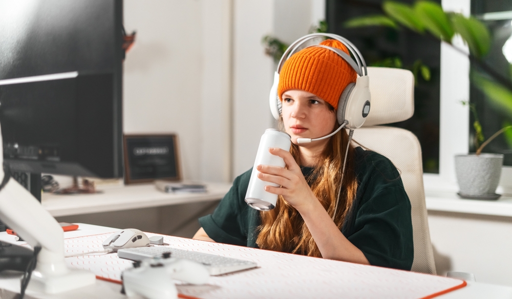 Gamer girl takes break from an intense gaming session, sitting her computer desk in cozy chair while sipping energy drink. Concept digital hobby and love for video games, fueled by caffeine and focus