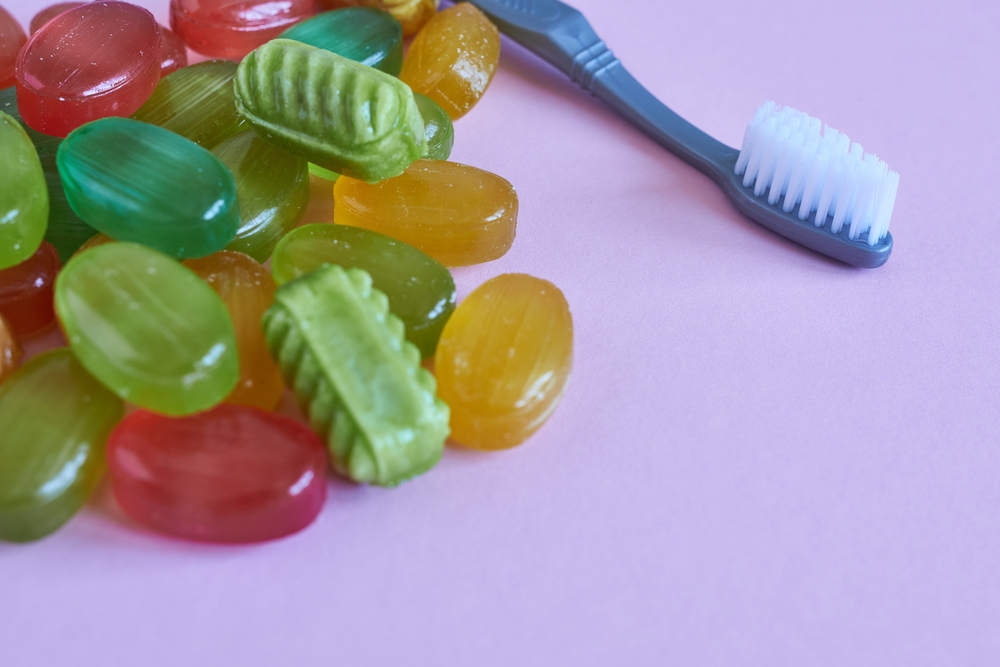 Lollipop candy and toothbrush on pink background. Copy space. Concept - harm of sweets for teeth.
