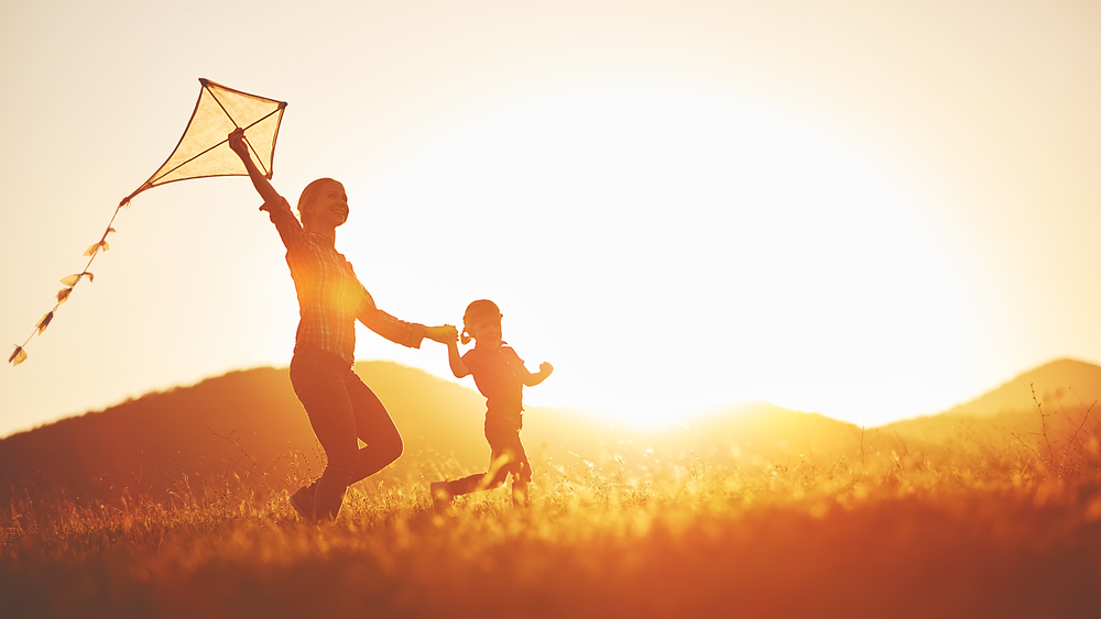 happy family mother and child run on meadow with a kite in the summer on the nature
