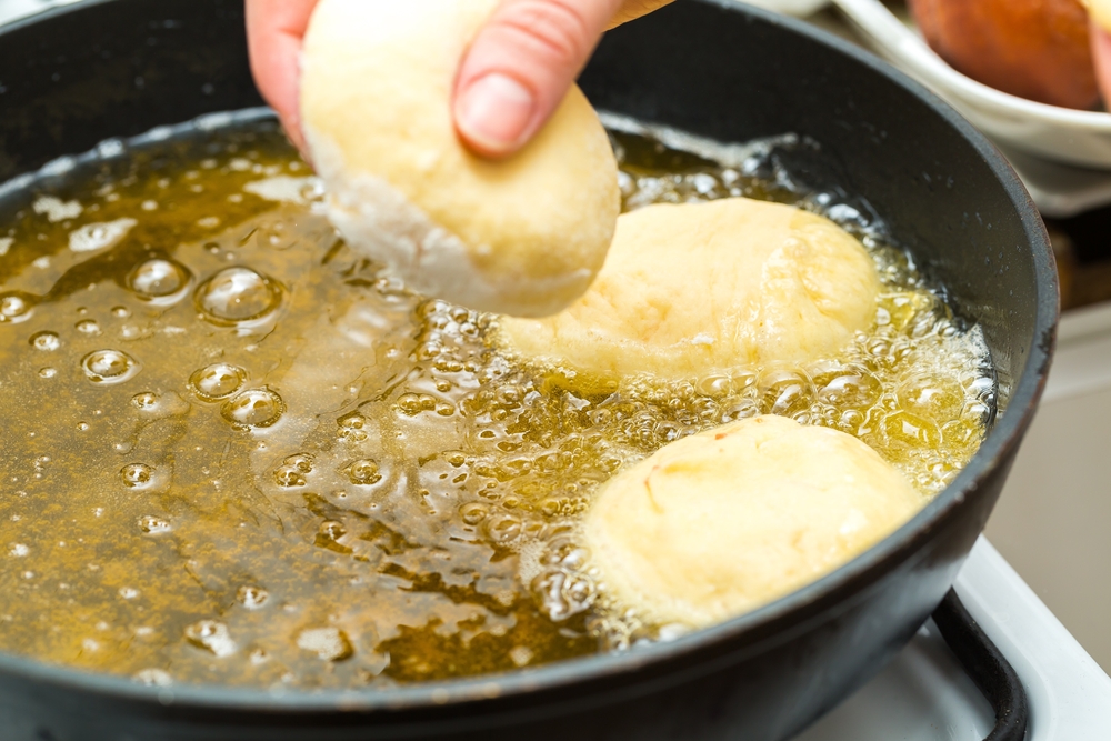Donuts frying in deep fat. Preparation of traditional donuts. Frying pan with fat and woman hands over pan.
