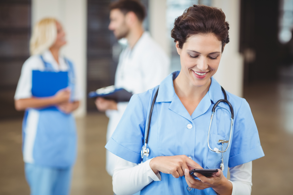 Nurse using on mobile phone with doctors discussing on background

