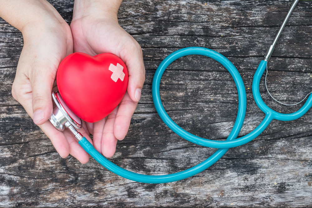 Healthcare medical insurance business, world heart health day, cardiovascular disease awareness month concept with red heart and bandage (band-aid) on woman's hands support with doctor's stethoscope
