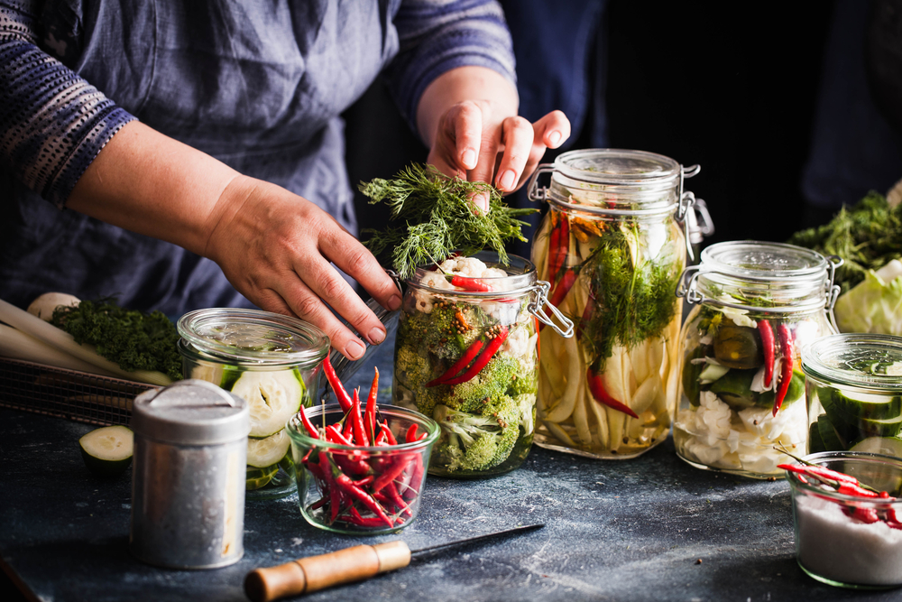 Pickled vegetables in jars displayed on table cauliflower broccoli bean cucumber green tomatoes fermented process glass jars variety copy space
