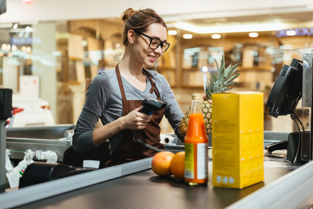 Smiling female cashier scanning grocery items at supermarket

