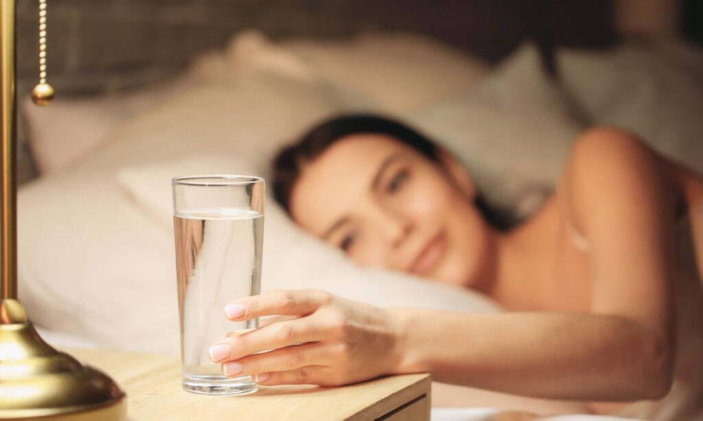 woman reaching for glass of water in bed