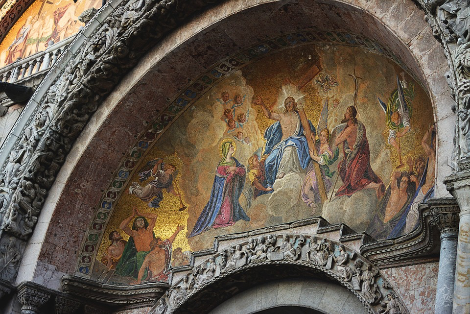 A Byzantine or medieval mosaic arch depicting Jesus Christ enthroned in heaven surrounded by saints and angels. The artwork is golden and ornate, typical of church decoration, showing Christ in blue robes with figures below looking upward toward him.