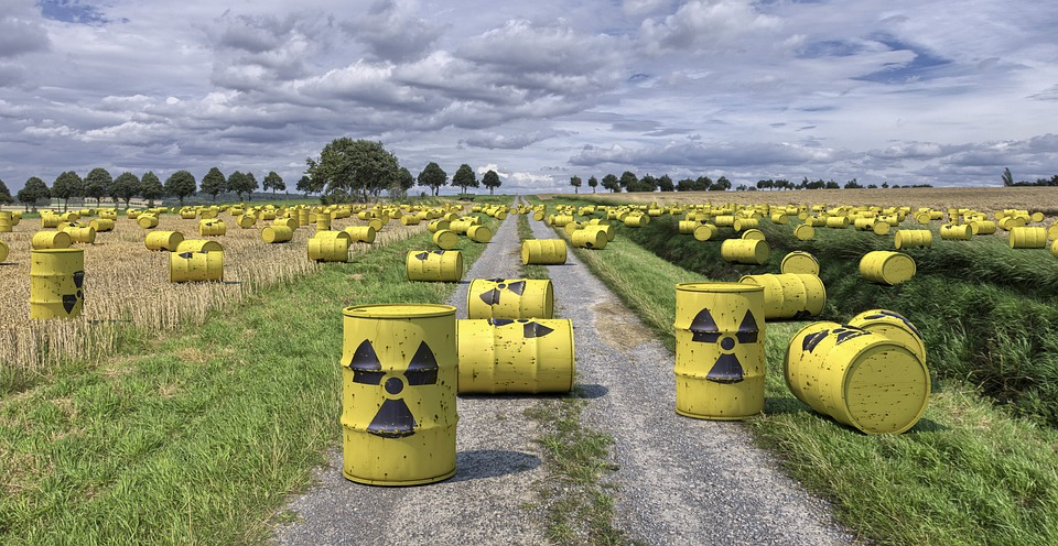Field with yellow nuclear waste barrels marked with radiation symbols, depicting the original threat of nuclear conflict that Gates worried about in his youth and that remains a concern for younger generations today.