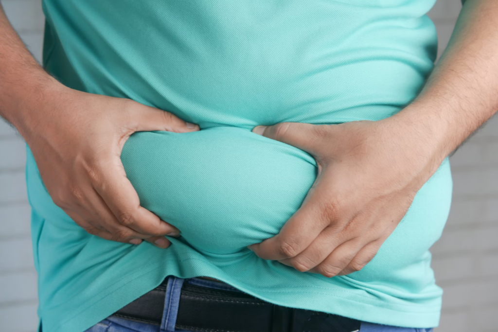 A person in a turquoise shirt gripping excess belly fat.