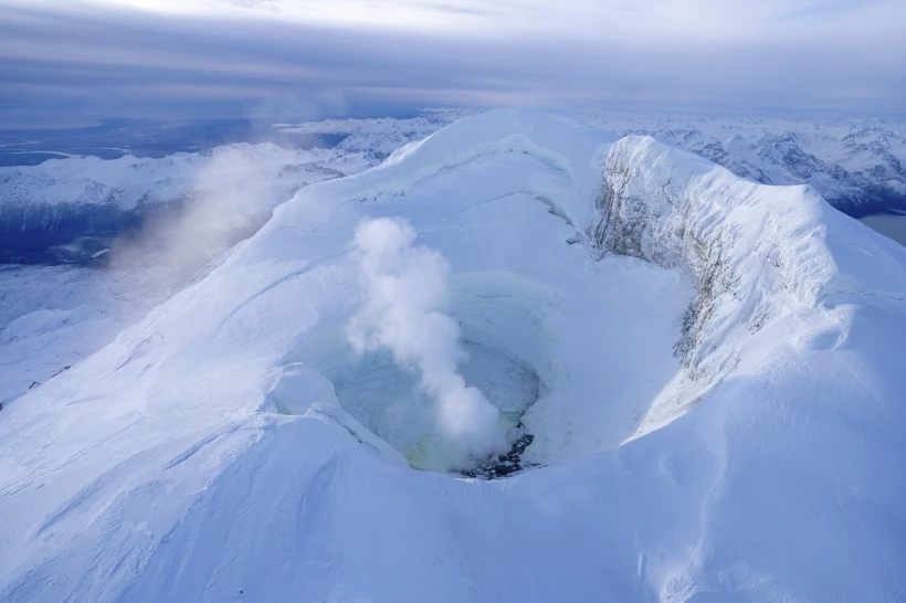 Ariel image of the snow covered Mount Spurr with smoke coming from the center.