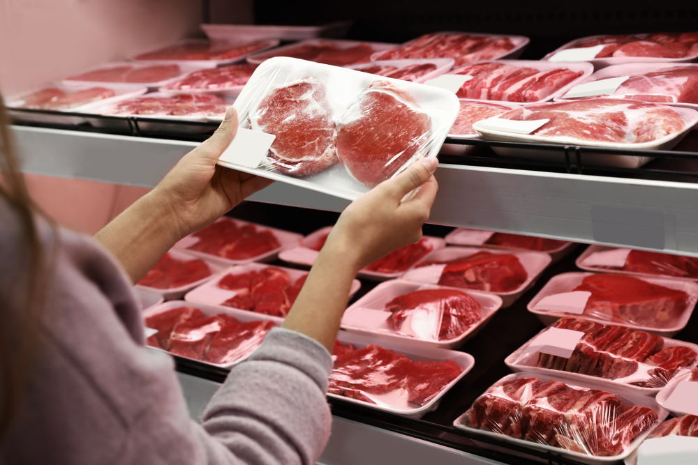 Woman taking packed pork meat from shelf in supermarket
