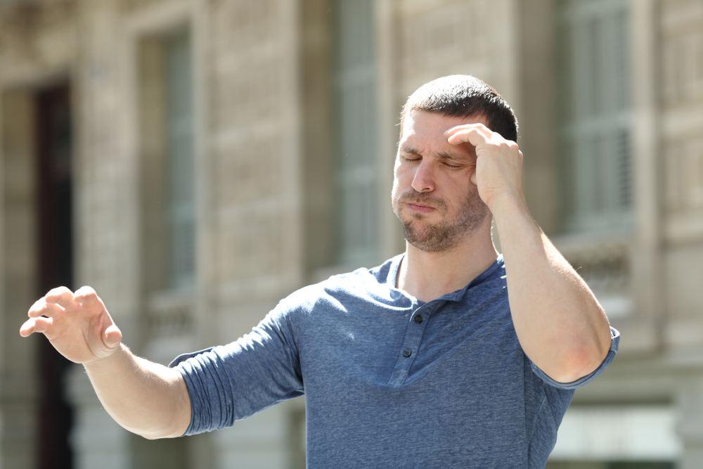 Dizzy adult man suffering headache trying to stay standing in the street
