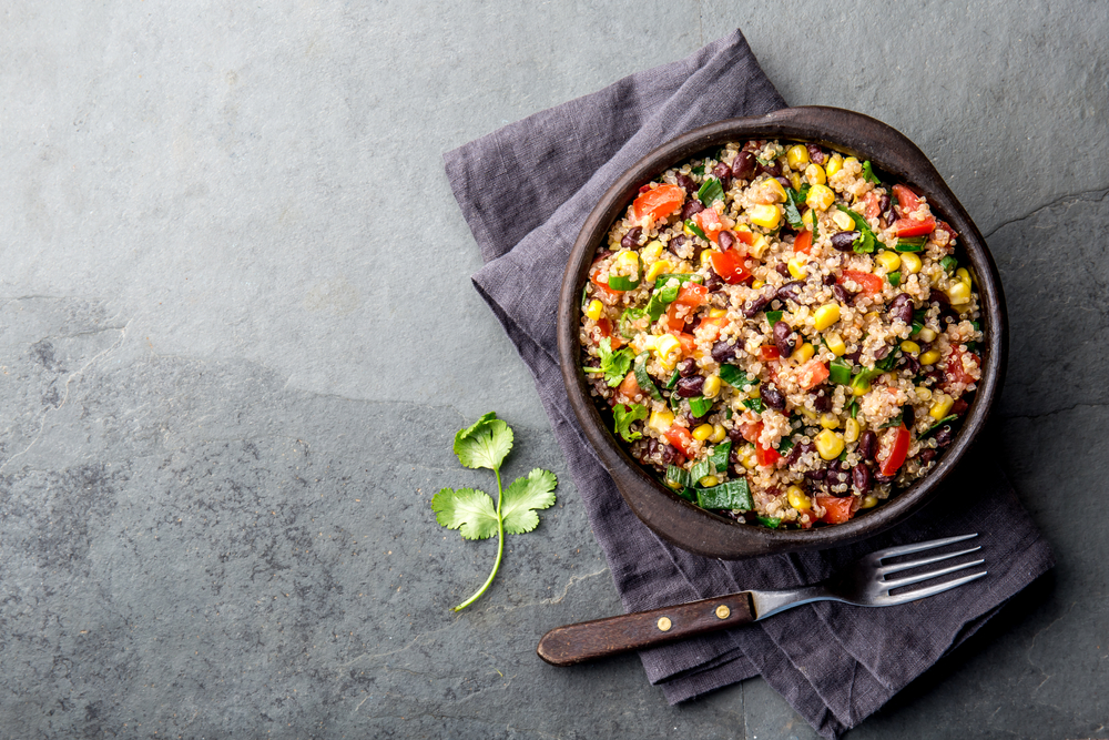 Mexican black bean corn quinoa salad in clay bowl top view, copy space.
