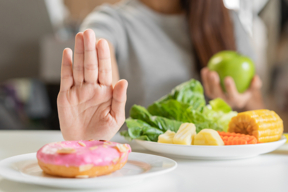 Diet, Dieting young asian woman or girl use hand push out, deny sweet donut and choose green apple, salad vegetables, eat food for good healthy, health when hungry. Close up female weight loss person.
