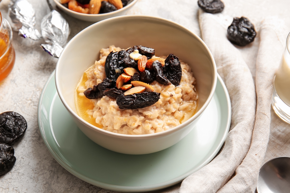 Tasty oatmeal with prunes and almond nuts in bowl on light table
