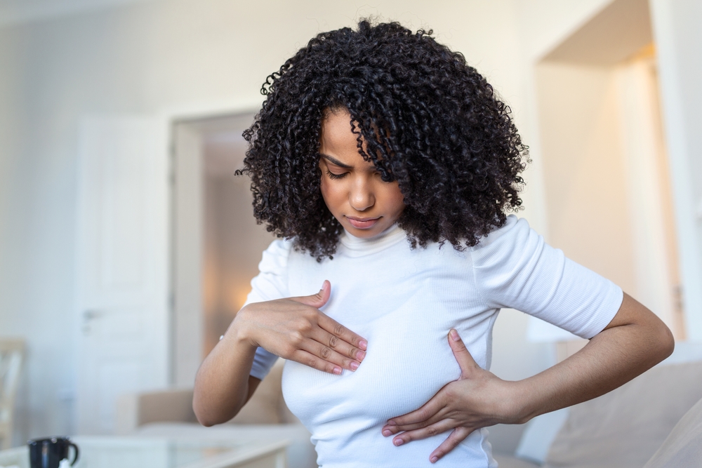 Young African American woman palpating her breast by herself that she concern about breast cancer. Healthcare and breast cancer concept
