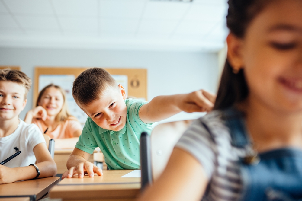 Children in the classroom at the lesson. Smiling boy passing note in class. Concept of the relationship of children at school.
