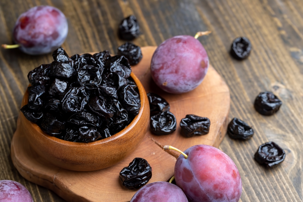 Black pile of prunes from a large number of ripe plums, a pile of prunes on a wooden table in the kitchen close-up
