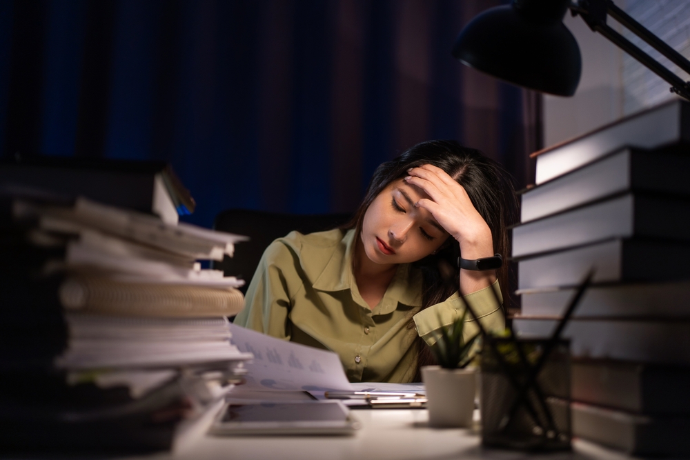 Portrait of Asian Businesswoman sitting and working hard at with front of computer and lots of documents on the table in workplace at late with serious action, Work hard and too late concept
