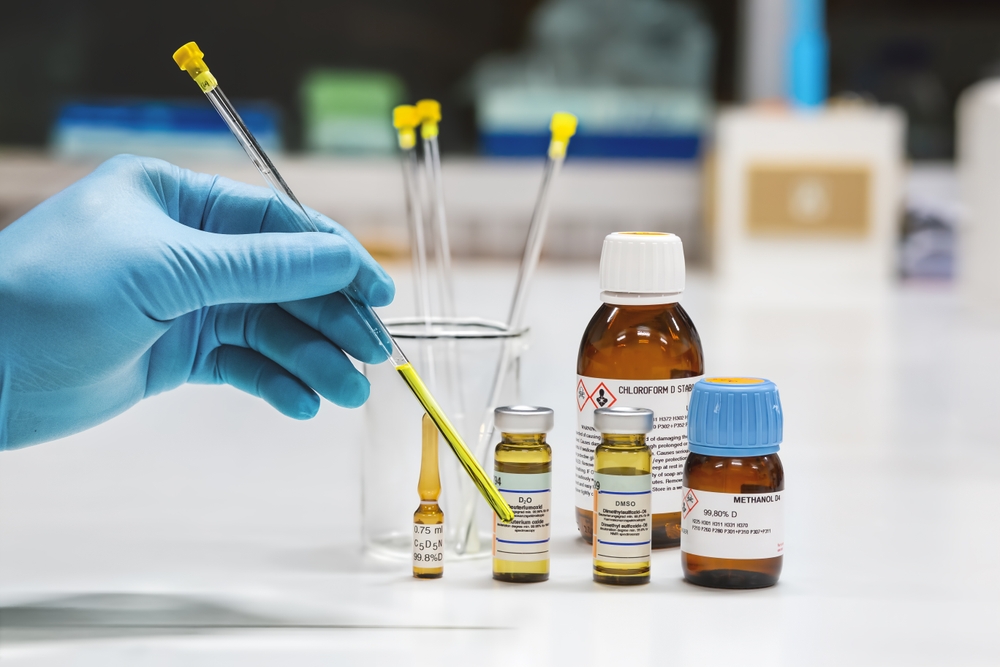 Hand of scientist shows yellow sample solution was prepared in NMR glass tubes for analysis by the NMR spectroscopy method. NMR solvent glass bottles, chloroform, pyridine, DMSO, D2O, and methanol.
