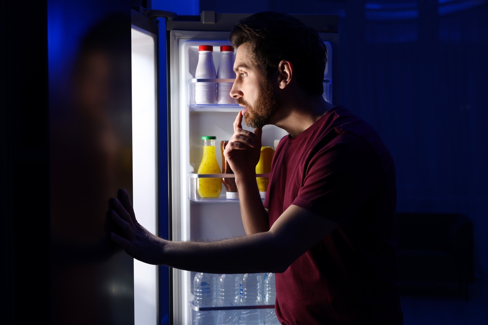 Man choosing food from refrigerator in kitchen at night. Bad habit