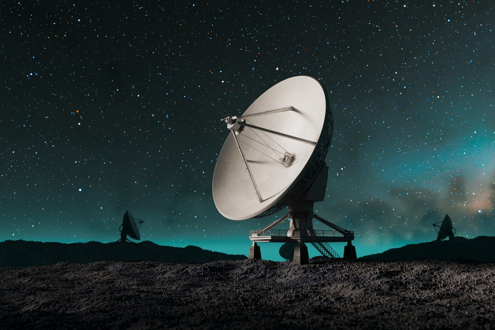 An array of large-scale radio telescopes meticulously scans the vastness of the starry nocturnal heavens, poised on rugged terrain, capturing cosmic phenomena.
