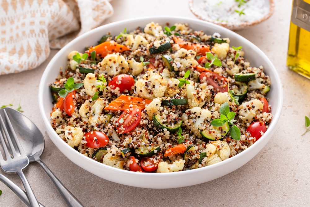 Delicious and nutritious quinoa salad with roasted vegetables, fresh tomatoes and herbs on a kitchen table
