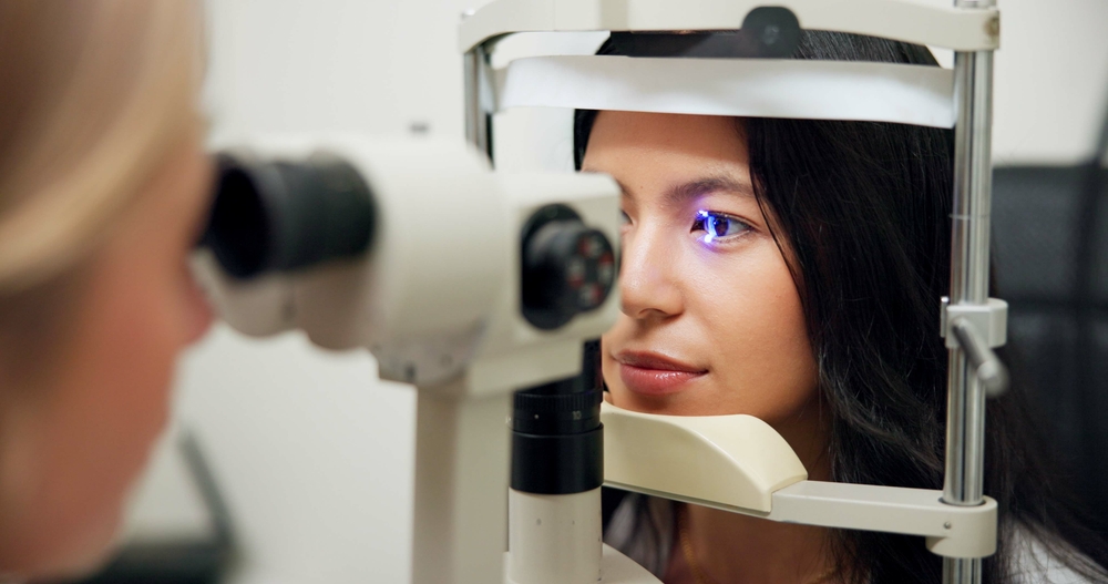 Woman, optometry and slit lamp for test, vision or care for wellness assessment with health in clinic. Doctor, optician and patient by machine, light and laser for retina scan with lens for eye exam
