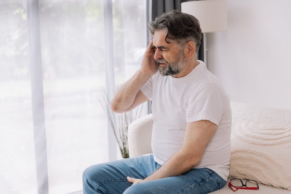 Home, senior man and headache on sofa for stress, emotional conflict and temporal vertigo. Living room, couch and old person with pain, migraine and anxiety due overthinking in retirement in house