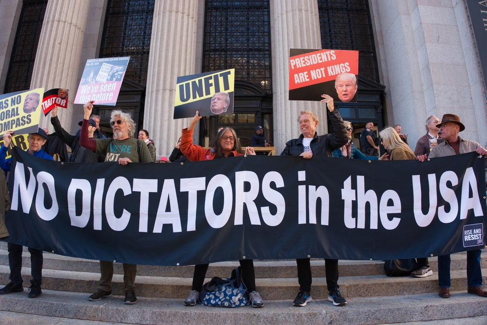New York, NY, USA - Oct 27, 2024: Protesters on building steps with “NO DICTATORS in the USA” banner and anti-Trump signs like “UNFIT” and “TRAITOR.” Rally opposes Trump’s political return.