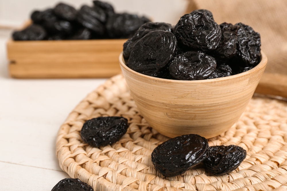 Bowl and box with dried prunes on white wooden background
