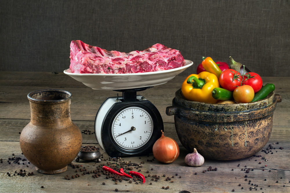 The meat on the scales, vegetables and pottery on a wooden table

